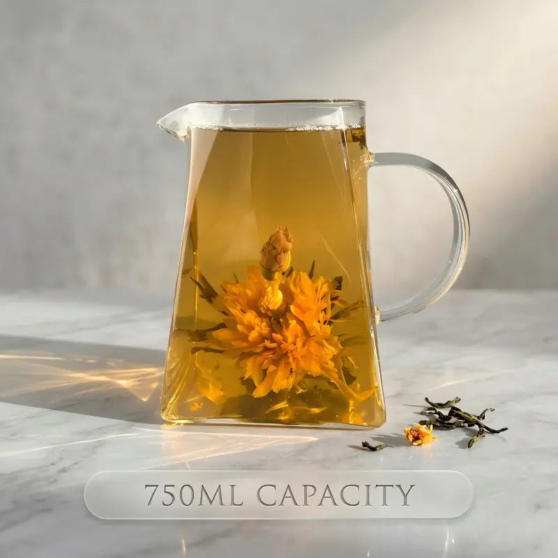 Clear glass pitcher filled with yellow liquid and flowers on a marble surface.